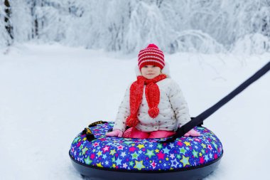 Kar tüpündeki mutlu, sağlıklı küçük kız. Sevimli küçük mutlu çocuk renkli lastiklerle kışın dışarıda eğleniyor. Aile yürüyüşü, karlı ormanda yürüyüş, açık havada. Aktif boş zaman