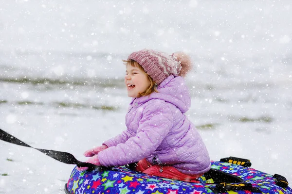 Active toddler girl sliding down the hill on snow tube. Cute little happy child having fun outdoors in winter on sledge . Healthy excited kid tubing snowy downhill, family winter time. — Stock Photo, Image