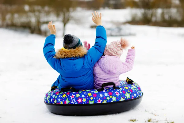 Aktivt småbarn flicka och skolpojke glider tillsammans ner för backen på snöslang. Barn, syskon har roligt utomhus på vintern på släde. Broder och syster slangar. Inget ansikte, oigenkännlig person — Stockfoto