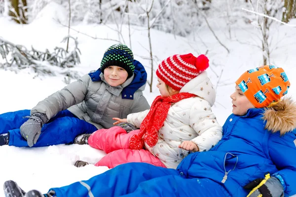 Zwei Schulkinder und ein kleines Mädchen im Winterwald. Glückliche Kinder, die sich im Winter im Freien mit Schnee vergnügen. Familie, drei Geschwister, Schwester und Brüder zusammen, draußen. Aktive Freizeit — Stockfoto