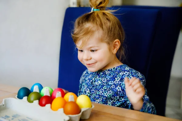 Excited little toddler girl coloring eggs for Easter. Child looking surprised at colored egg hoarding and celebrating catholic and christian holiday with family. Cute kid helping to color, indoors. — Stock Photo, Image