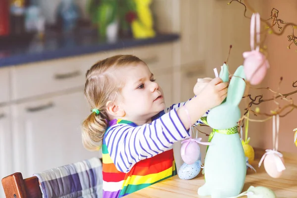 Ağaç süsleyen küçük şirin bir kız ve renkli pastel plastik yumurtalarla tavşan. Mutlu bebek Paskalya süslemeleriyle eğleniyor. Aile tatilinde gülümseyen sevimli çocuk. — Stok fotoğraf