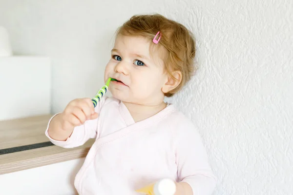 Menina bebê segurando escova de dentes e escovando os primeiros dentes. Criança aprendendo a limpar o dente de leite. Conceito de prevenção, higiene e saúde. Criança feliz no banheiro — Fotografia de Stock