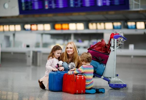 Zwei müde kleine Kinder, Junge und Mädchen, Geschwister und Mutter am Flughafen. Kinder, Familien, die mit dem Flugzeug in den Urlaub fliegen und mit dem Gepäckwagen mit Koffern am Terminal auf den Flug warten. — Stockfoto