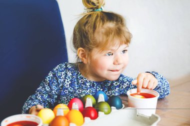 Heyecanlı küçük kız Paskalya için yumurta boyuyor. Çocuk, renkli yumurta stoklama ve Katolik ve Hıristiyan bayramını ailesiyle kutlamaya şaşırmış görünüyor. Hoş çocuk boyamaya yardım ediyor, içeride..