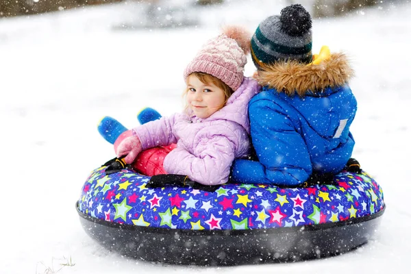 Active toddler girl and school boy sliding together down the hill on snow tube. Happy children, siblings having fun outdoors in winter on sledge. Brother and sister tubing snowy downhill, family time. — Stock Photo, Image