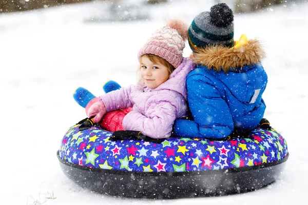 Niña activa y niño de la escuela deslizándose juntos por la colina en el tubo de nieve. Niños felices, hermanos divirtiéndose al aire libre en invierno en trineo. Hermano y hermana tubería nevado cuesta abajo, tiempo en familia. — Foto de Stock