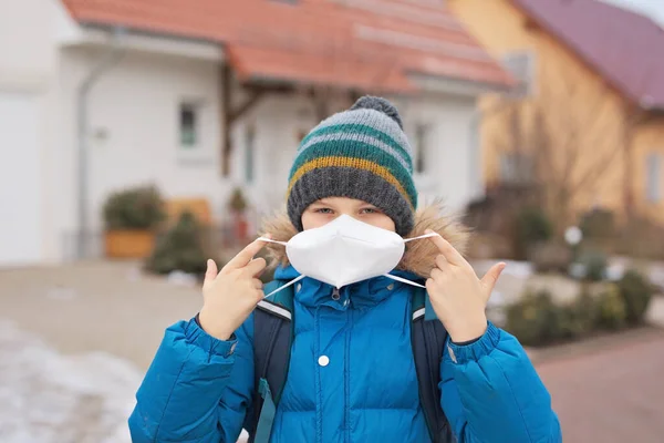 Kid boy wearing ffp medical mask on the way to school. Child backpack satchel. Schoolkid on cold autumn or winter day with warm clothes. Lockdown and quarantine time during corona pandemic disease — Stock Photo, Image