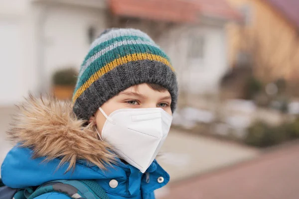 Kid boy wearing ffp medical mask on the way to school. Child backpack satchel. Schoolkid on cold autumn or winter day with warm clothes. Lockdown and quarantine time during corona pandemic disease — Stock Photo, Image