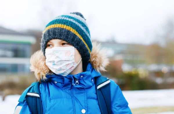 Niño con máscara médica ffp camino a la escuela. Mochila para niños. Colegial en otoño frío o día de invierno con ropa de abrigo. Tiempo de bloqueo y cuarentena durante la enfermedad pandémica de corona — Foto de Stock