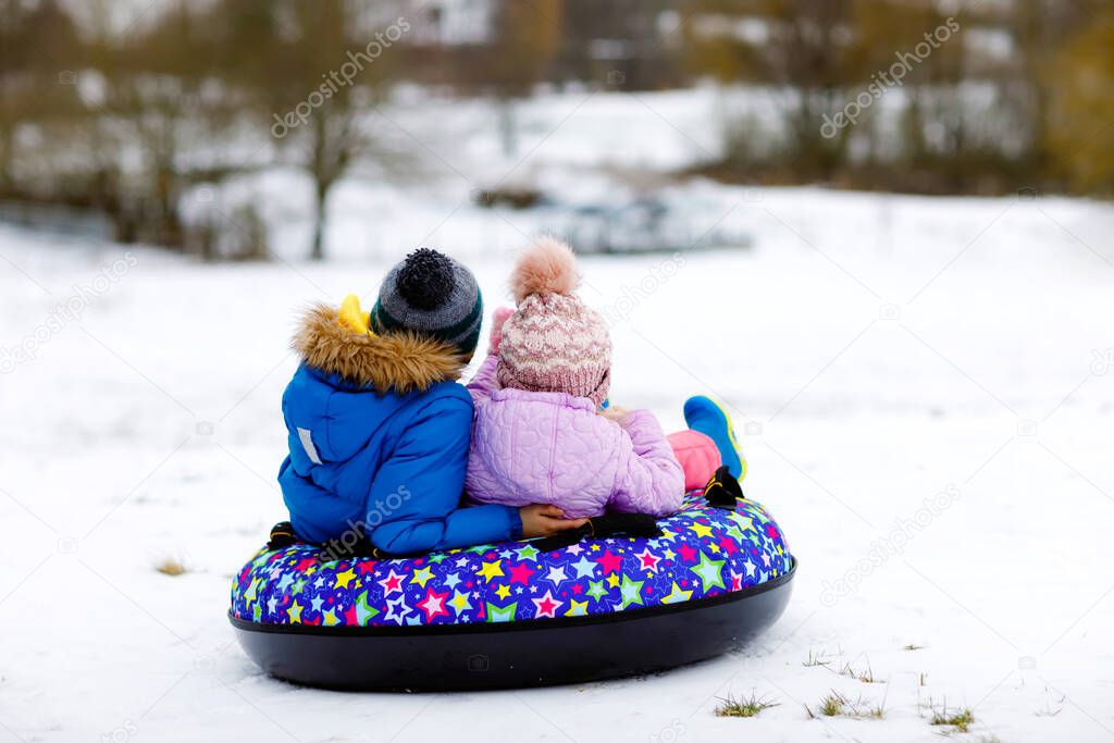 Active toddler girl and school boy sliding together down the hill on snow tube. Children, siblings having fun outdoors in winter on sledge. Brother and sister tubing. No face, unrecognizable person