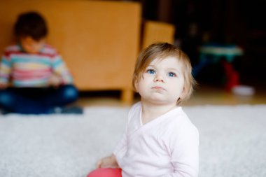 Evdeki sevimli kızın portresi. Küçük kız kameraya bakıyor ve gülümsüyor. Aile, yeni hayat, çocukluk, başlangıç konsepti. Kardeş çocuk arka planda.