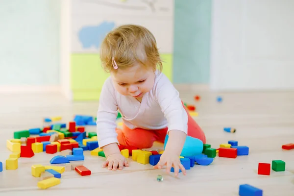 Мила маленька дівчинка грає з освітніми іграшками. Щаслива здорова дитина розважається з різними дерев'яними блоками вдома або в дитячій кімнаті. Повзання дитини і вивчення кольорів і форм, в приміщенні — стокове фото