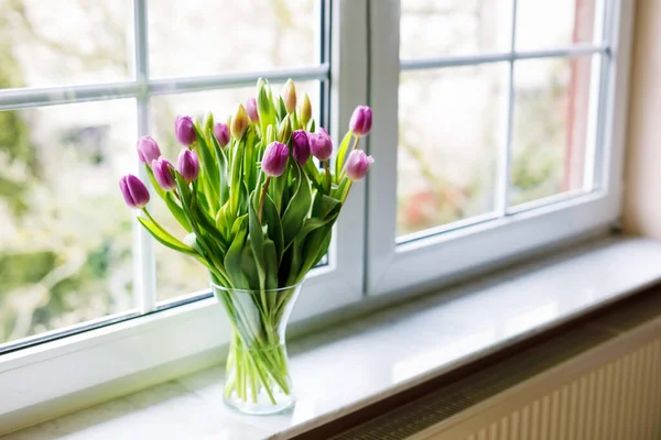 Hromada tulipánových květin ve váze u okna. Krásné kvetoucí tulipány na Valentýna nebo Den matek nebo narozeniny. Domácí dekorace. — Stock fotografie