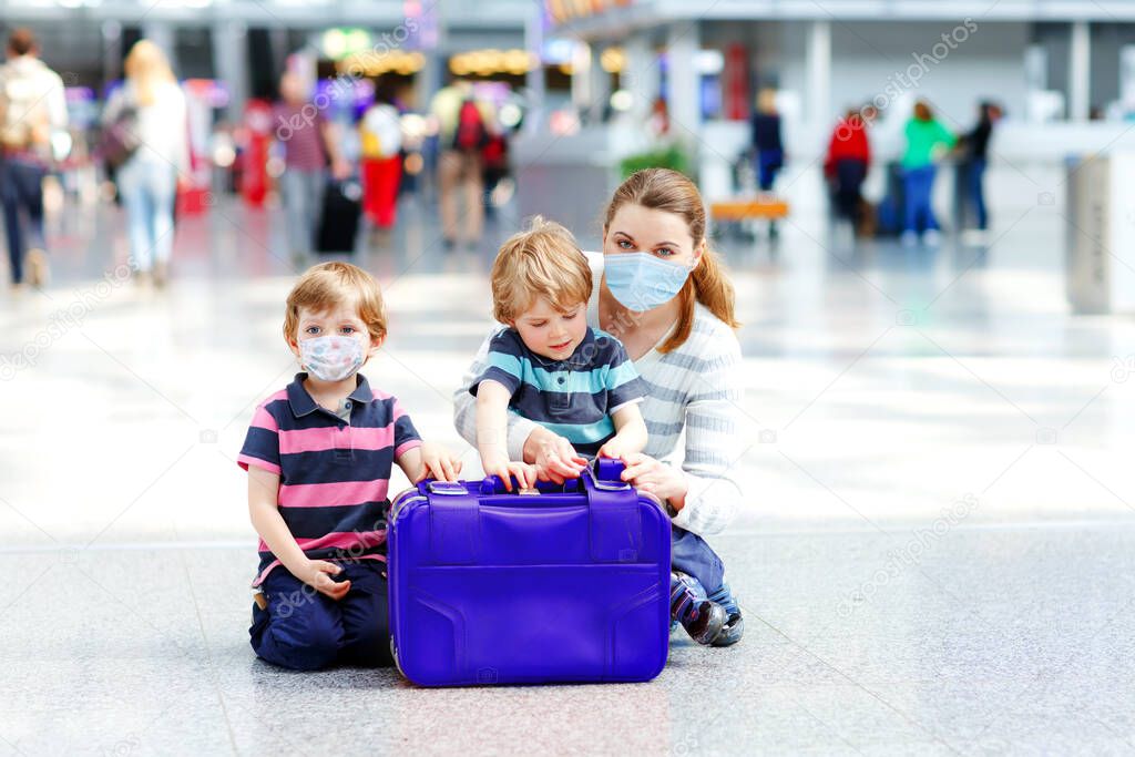 Two little kids, preschool siblings boys and mother in medical mask at airport. Children and woman, family travel by plane during corona virus pandemic lockdown. People in mask as covid protection