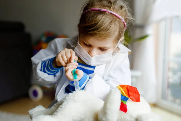 Pequena menina faz injeção para ursinho de pelúcia. Criança bonito com máscara médica jogando médico, segurando seringa com vacina. Conceito de vacinação vívida pelo vírus da coronária. — Fotografia de Stock