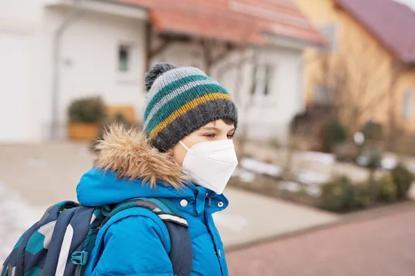 Хлопчик одягнений у медичну маску по дорозі до школи. Дитячий рюкзак. Школярка в холодний осінній або зимовий день з теплим одягом. Блокування і карантинний час під час пандемії корона — стокове фото