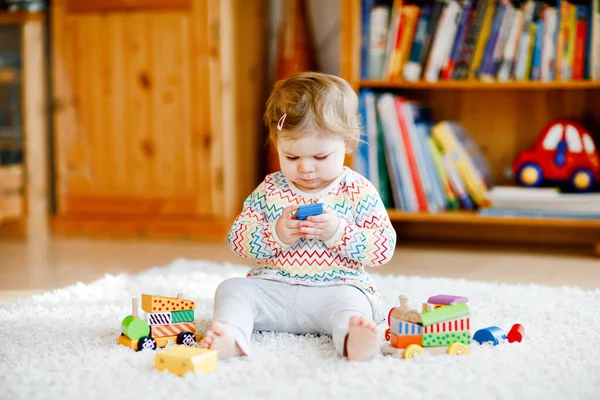 Pequena menina brincando com brinquedos educativos de madeira em casa ou berçário. Criança com trem colorido. Criança se divertindo com brinquedos diferentes. Criança solitária durante quarentena pandêmica do vírus da corona — Fotografia de Stock