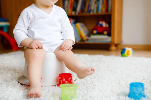 Closeup of cute little old toddler baby girl child sitting on potty. Kid playing with educational toy and Toilet training concept. Baby learning, development steps. No face, unrecognizable person.