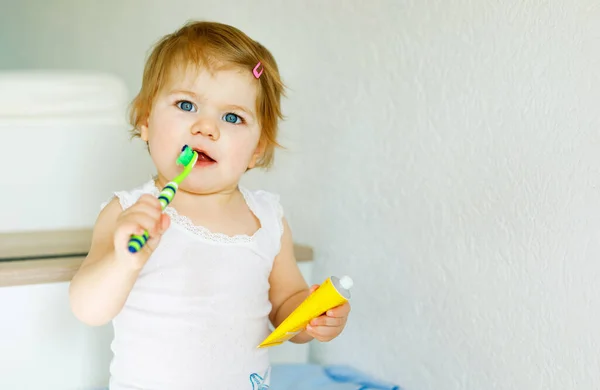 Niña sosteniendo cepillo de dientes y cepillándose los primeros dientes. Niño aprendiendo a limpiar los dientes de leche. Concepto de prevención, higiene y salud. Niño feliz en el baño — Foto de Stock