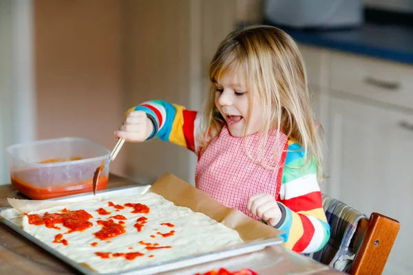 Adorable little toddler girl making italian pizza at home. Cute happy child having fun in home kitchen, indoors. Kid, preschooler helping and preparing healthy meal — Stock Photo, Image