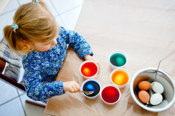 Primo piano della bambina che colora le uova per Pasqua. Primo piano del bambino che guarda sorpreso le uova colorate colorate, celebrando la vacanza con la famiglia. Dall'alto, volto non riconosciuto. — Foto Stock