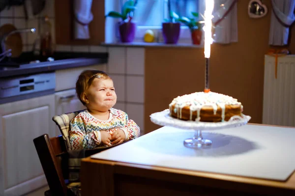 Милая плачущая маленькая девочка празднует первый день рождения. Ребенок боится фейерверков на выпечке, в помещении. Недовольство тошнотворным шилом — стоковое фото