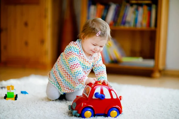 Klein meisje dat thuis of in de kinderkamer met educatief houten speelgoed speelt. Peuter met kleurrijke rode auto. Kind heeft plezier met ander speelgoed. Eenzame jongen tijdens corona virus pandemische quarantaine — Stockfoto