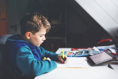 Okul çocuğu evde okul için tabletle öğreniyor. Ev ödevi yapan, ped kullanan ve modern aletler kullanan sevimli bir çocuk. Evde eğitim ve uzaklık öğrenme kavramı.