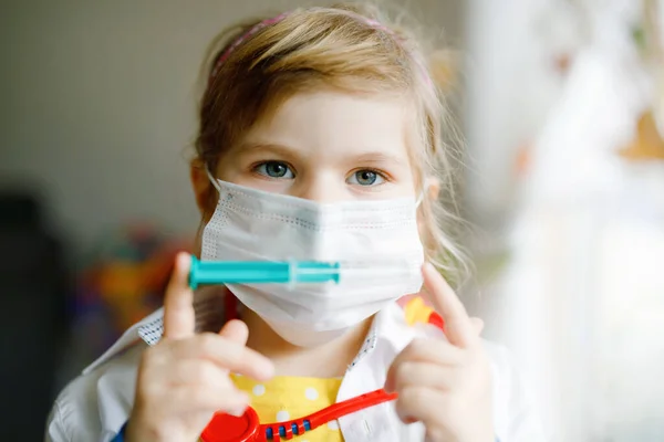 La niña se inyecta. Lindo niño con máscara médica jugando al médico, sosteniendo la jeringa con la vacuna. Concepto de vacunación covid contra el Coronavirus. Juego de rol de niño en casa. —  Fotos de Stock