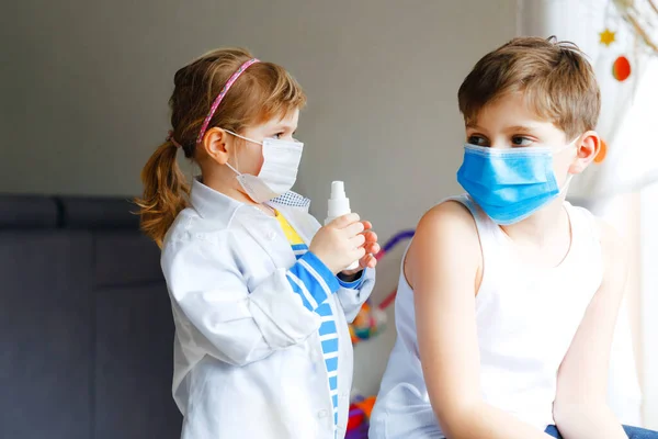 La niña le inyecta al hermano, al chico de la escuela. Niños, hermanos con máscara médica jugando al doctor, sosteniendo jeringa con vacuna. Concepto de vacunación covid contra el Coronavirus. Los niños juegan papel juego —  Fotos de Stock