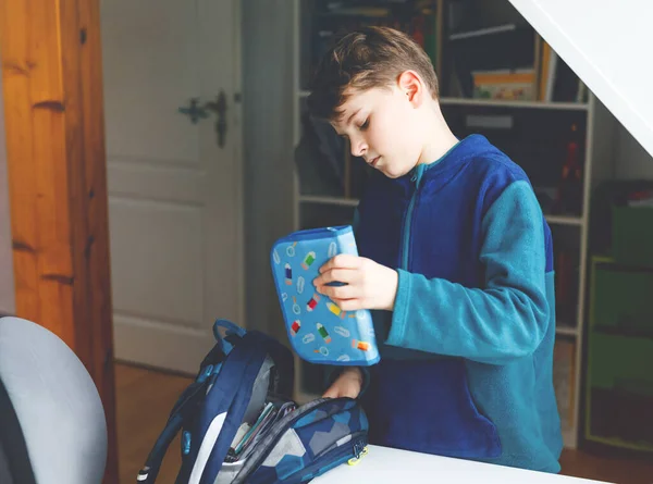 Rapaz da escola a preparar-se de manhã para a escola. Criança saudável enchendo sacola com livros, canetas, pastas e material escolar. Preparação, conceito de rotina. — Fotografia de Stock