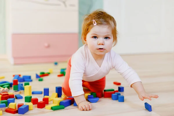 Eğitici oyuncaklarla oynayan tatlı küçük bir kız. Mutlu sağlıklı çocuk evde ya da çocuk odasında renkli tahta bloklarla eğleniyor. Bebek sürünüyor, renkleri ve biçimleri öğreniyor. — Stok fotoğraf