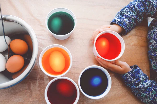 Closeup of little toddler girl coloring eggs for Easter. Close-up of child looking surprised at colorful colored eggs, celebrating holiday with family. From above, unrecognized face. — Stock Photo, Image