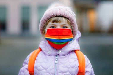 Anaokuluna, çocuk parkına ya da kreşe giderken maske takan küçük bir çocuk. Soğuk bir günde sırt çantalı bir çocuk ve sıcak giysiler. Corona salgını sırasında tecrit ve karantina süresi