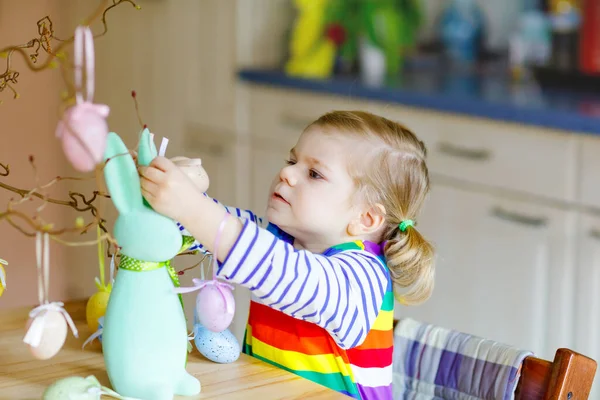 나무를 장식하는 귀여운 꼬마 여자 애와 색깔이 있는 파스텔 플라스틱 알을 가진 토끼. 부활절 장식을 즐기는 행복 한 아기. 가족 휴가를 즐기며 다정하게 웃는 건강 한 아이 — 스톡 사진