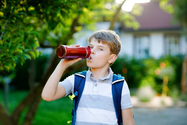 Niño feliz bebiendo de botella de agua y mochila o mochila. Un colegial de camino a la escuela. Un niño sano al aire libre. Regreso a la escuela. —  Fotos de Stock