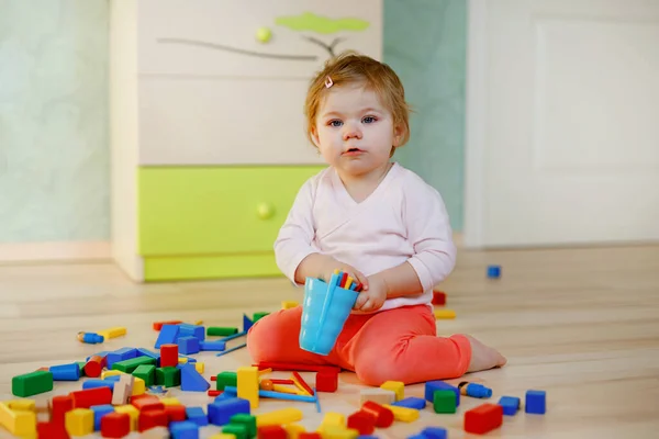 Eğitici oyuncaklarla oynayan tatlı küçük bir kız. Mutlu sağlıklı çocuk evde ya da çocuk odasında renkli tahta bloklarla eğleniyor. Bebek sürünüyor, renkleri ve biçimleri öğreniyor. — Stok fotoğraf