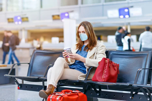 Een vrouw met een medisch masker die boek leest en koffie drinkt. Vrouw wachtend op vlucht zittend in bijna lege internationale luchthaventerminal als gevolg van coronavirus pandemische reisbeperkingen Stockfoto