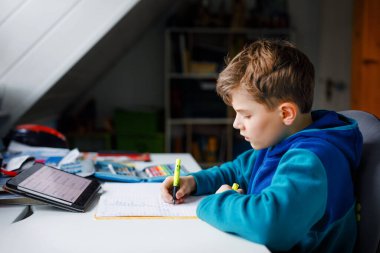 Okul çocuğu evde okul için tabletle öğreniyor. Ev ödevi yapan, ped kullanan ve modern aletler kullanan sevimli bir çocuk. Evde eğitim ve uzaklık öğrenme kavramı.