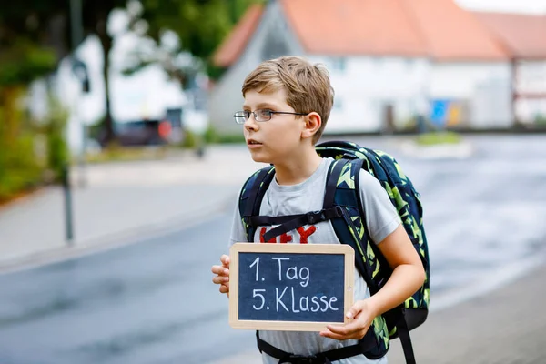 Glücklicher kleiner Junge mit Brille und Rucksack oder Schulranzen. Schulkind auf dem Weg zur Mittel- oder Oberschule. Kind auf der Straße. Zurück zur Schule. Am ersten Tag Fünfte Klasse auf Deutsch. — Stockfoto