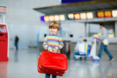 Uluslararası havaalanındaki terminalde büyük bavulları olan küçük mutlu çocuk. Okul öncesi heyecanlı çocuk uçuşu ve tatile çıkmayı bekliyor. Seyahat aile hayatı..