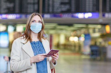 Uluslararası havaalanında maskeli bir kadın elektronik panoyu kontrol ediyor ve uçuş için bekliyor. Coronavirus seyahat kısıtlamaları nedeniyle Avrupa pasaportlu kadın yolcu