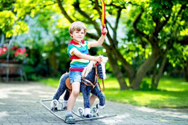 Küçük çocuk bir yaz parkında oyuncak atıyla oynuyor. Mutlu gülümseyen çocuk dışarıda eğleniyor. 5 yaşında sarışın bir çocuk.