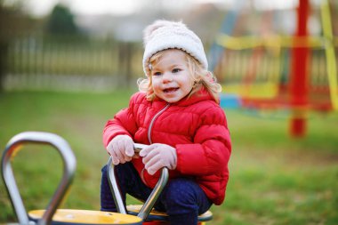 Küçük tatlı kız oyun alanında eğleniyor. Mutlu küçük çocuk tırmanışı, farklı ekipmanların üzerinde sallanmak ve kaymak. Renkli giysiler içinde soğuk bir günde. Çocuklar için aktif açık hava oyunu