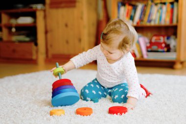 Evde ya da çocuk odasında eğitici tahta oyuncaklarla oynayan sevimli, güzel bir kız bebek. Renkli yığınla piramidi ve müzik oyuncağı olan bir bebek. Mutlu sağlıklı çocuk farklı oyuncaklarla eğleniyor.