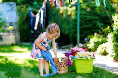 Küçük kız çamaşırları asıyor, bahçede kurutmak için temiz elbiseler ve pantolonlar, çamaşır yaptıktan sonra dışarıda. Mutlu çocuk ev işlerine yardım ediyor. Aile birlikte çalışıyor, çocuk yardım etmeyi öğreniyor..