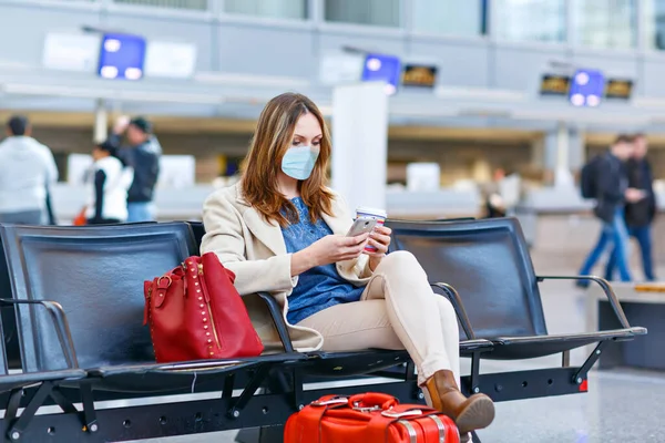 Mujer con máscara médica con smartphone y café. Mujer molesto por cancelación de vuelo, sentado en la terminal vacía del aeropuerto internacional debido a las restricciones de viaje pandémica coronavirus Imagen de stock