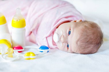 Hemşire şişeleri, çıngırağı ve emziği olan yeni doğmuş tatlı bir kız bebek. Bebekler için formül içeceği. Yeni doğmuş bir çocuk, yatakta yatan küçük bir kız. Aile, yeni hayat, çocukluk, başlangıç, şişe besleme konsepti