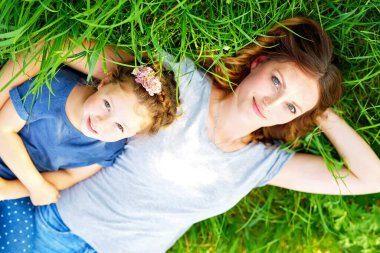 Güzel anne ve küçük kız yeşil çimlerde oturuyor ve dinleniyorlar.